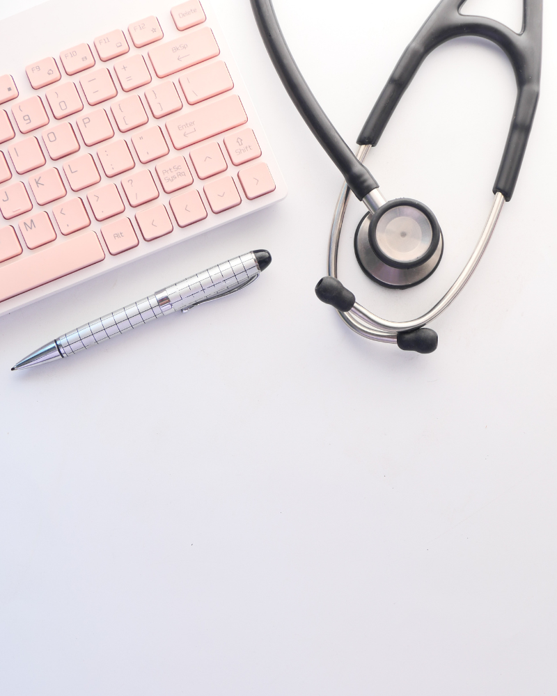 A light pink keyboard on a grey background with a pen below the keyboard and a stethoscope to the right