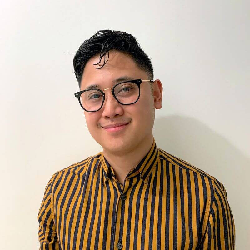 A headshot of Patrick, smiling into the camera with short black hair, wearing a yellow and black striped shirt.