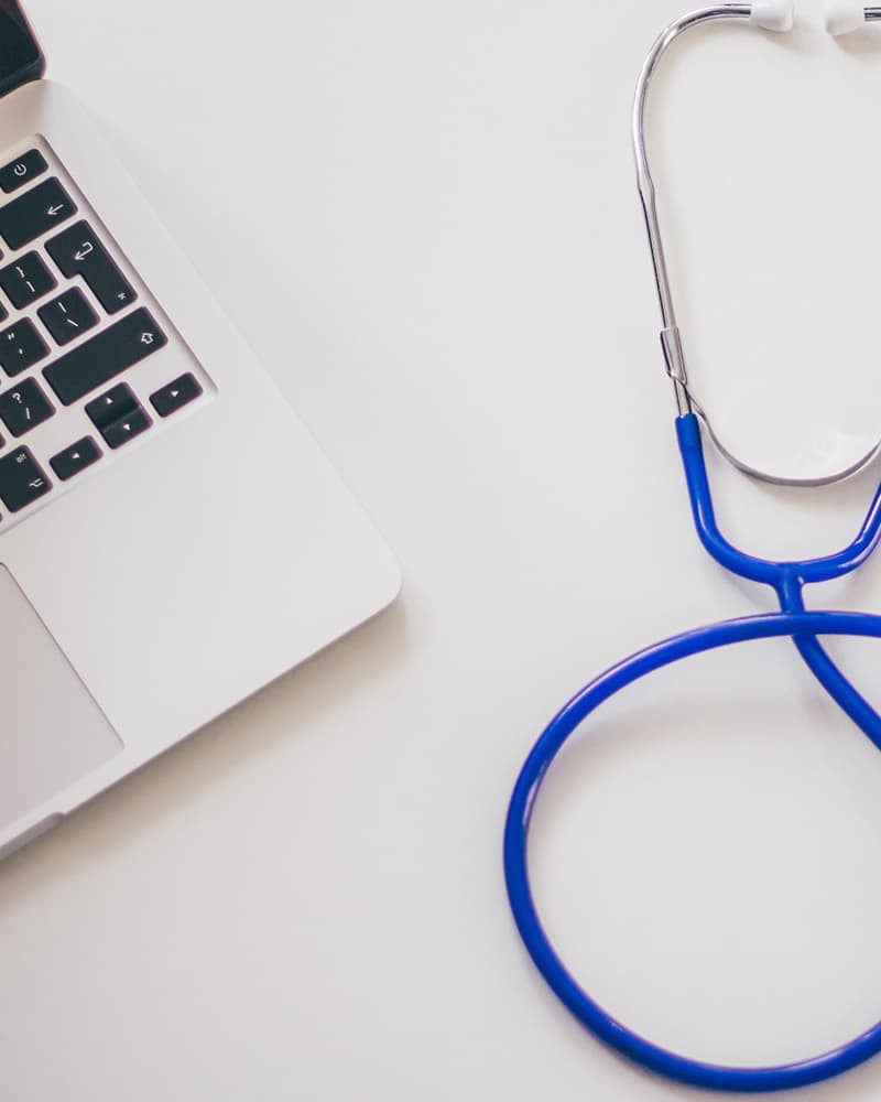 A blue stethoscope and a laptop computer sitting on a counter.
