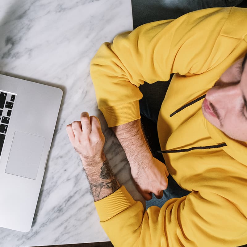 A person with a yellow sweater and tattoos speaking to someone digitally over a laptop computer.