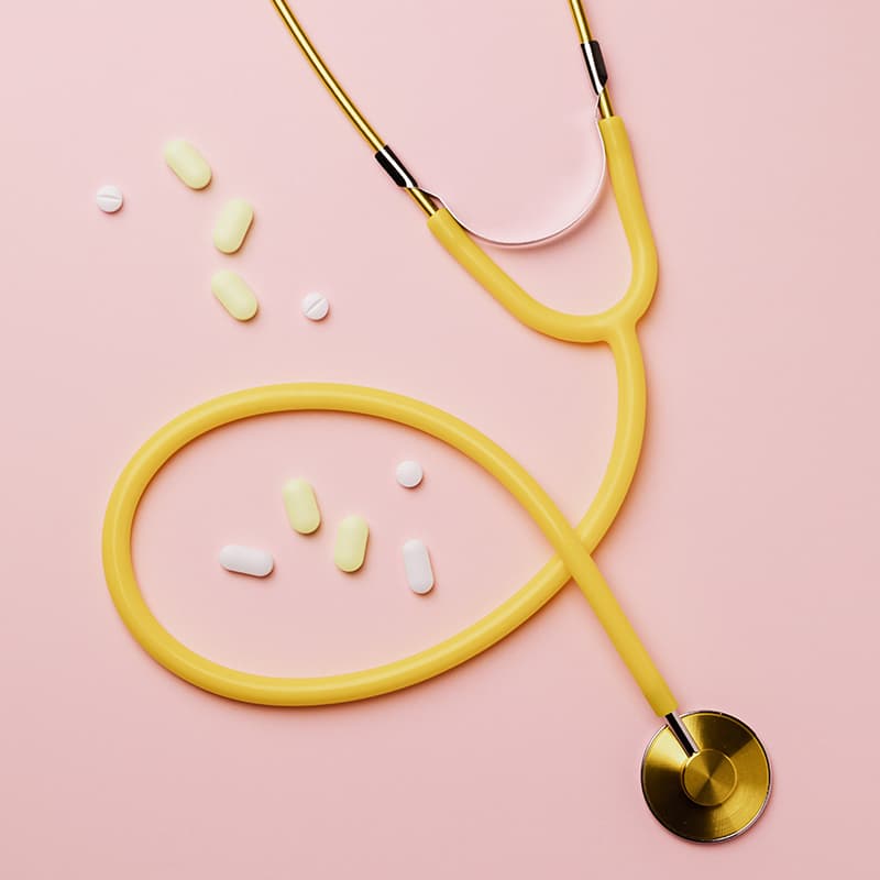 A yellow stethoscope and some yellow and white pills on a pink background.